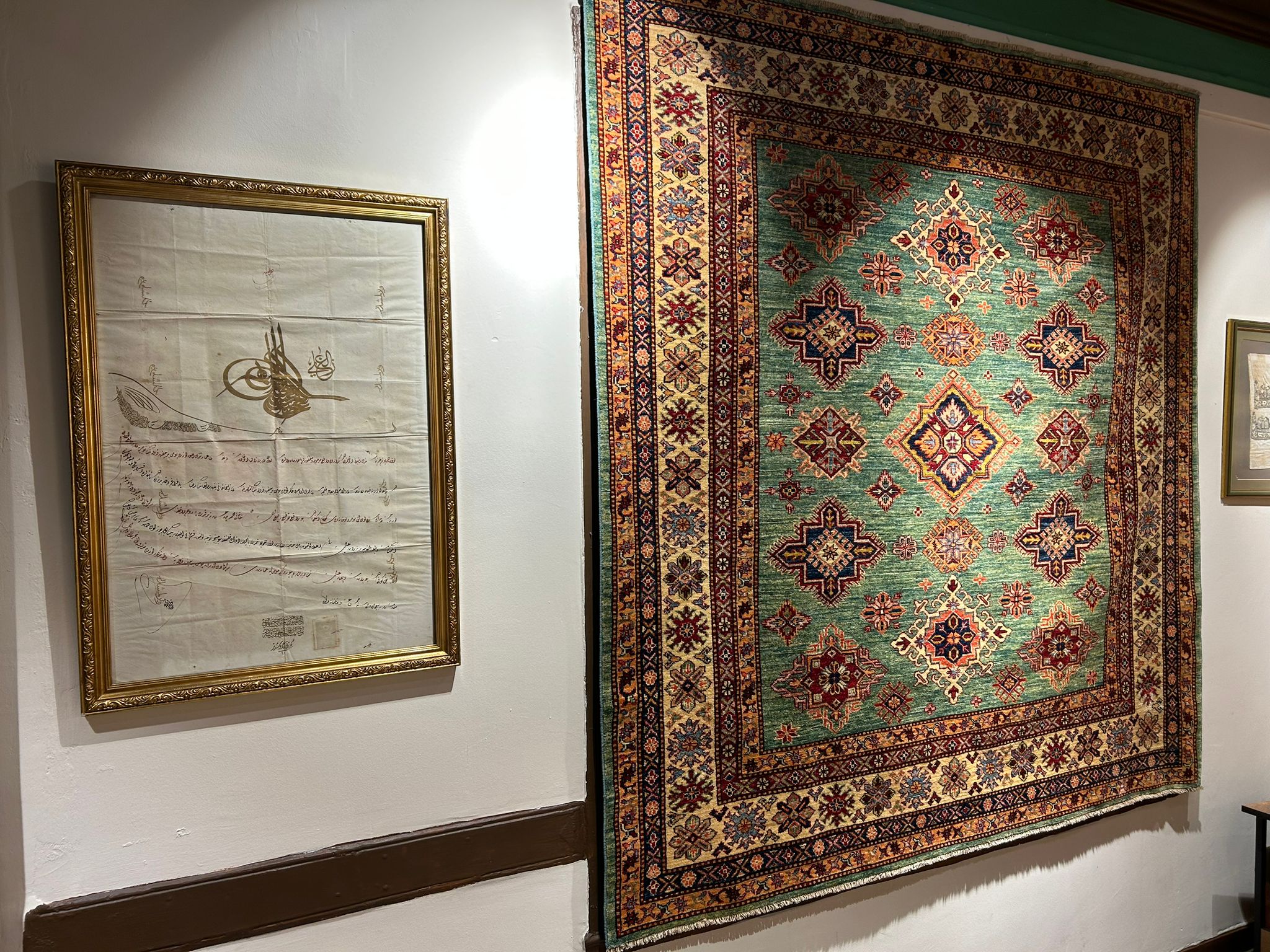 A rug hung beside a framed document on a wall inside Gordes